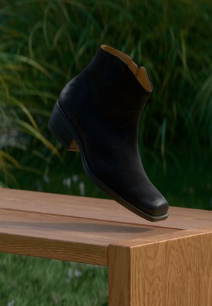 Bottine noire en cuir flottant au-dessus d'un banc en bois avec des plantes vertes floues en arrière-plan.