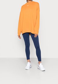 Orange oversized sweatshirt med en vit logotyp, kombinerat med marina leggings och vita sneakers. Slätt tyg och avslappnad passform.