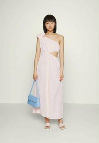 Vestido assimétrico rosa com um ombro, detalhe recortado e acabamento de flor drapeada. Combinado com uma mala azul claro e sandálias bege.