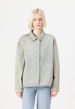 Light blue denim jacket with a wide collar, front buttons, and dropped shoulders, featuring a relaxed fit and minimal stitching details.