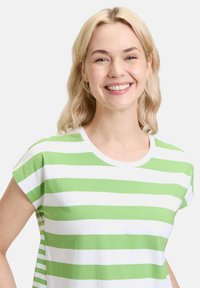 Zielona i biała koszulka w paski z okrągłym dekoltem, krótkimi rękawami i miękkim bawełnianym materiałem. Paski są równo rozmieszczone i żywe.