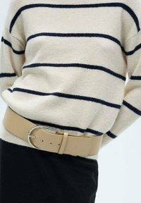Beige leather belt with a large, silver circular buckle, worn over a striped cream sweater, featuring navy horizontal lines.