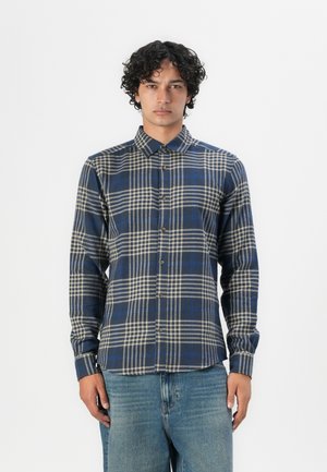 Camisa de cuadros azul y beige de manga larga con un diseño de botones, cuello tipo solapa y tejido texturizado. Llevada con jeans de mezclilla azul.