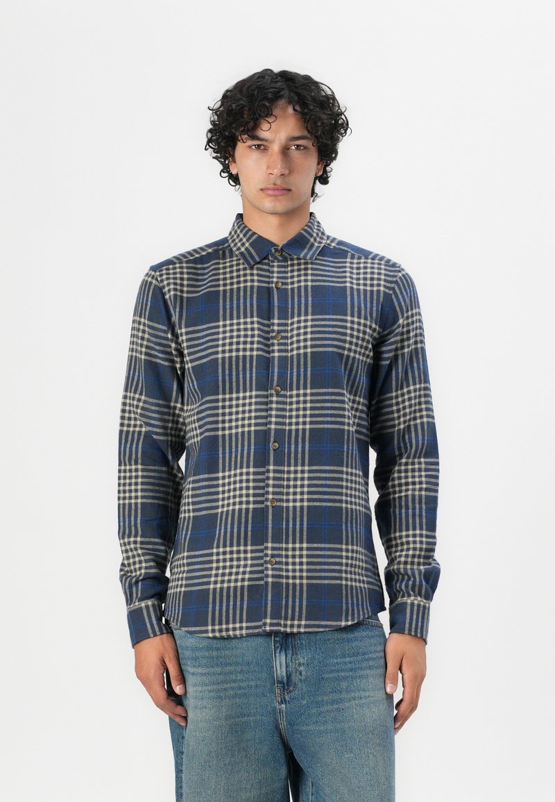 Blau-beige karierter Langarmshirt mit einer Knopfverschluss-Design, Kragen und strukturiertem Stoff. Getragen mit blauen Jeans.