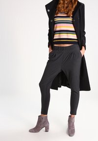 Grijze taps toelopende broek met een elastische tailleband, gecombineerd met een multi-kleurige gestreepte cropped trui en grijze enkellaarsjes. Lange zwarte jas.