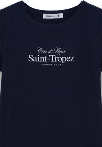 T-shirt a maniche corte blu navy in cotone. Presenta una scritta bianca: "Côte d'Azur Saint-Tropez TENNIS CLUB" in caratteri eleganti. Collo classico a giro.