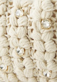 Beige woven textile with knotted texture, featuring circular, clear gems set in gold settings, adding contrast and detail.