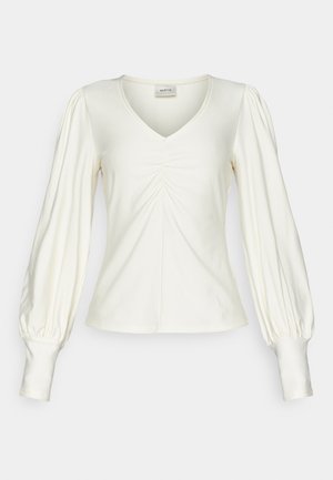 Cream-colored long-sleeve top with a V-neck, featuring gathered detailing at the front and puffy sleeves tapering at the cuffs.