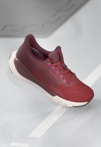 Pantofii sport roșii cu inserții din plasă, guler căptușit și detalii texturate. Talpa mediană și șireturile contrastante. Logo-ul vizibil pe lateral.