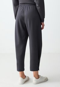 Dunkelgraue Jogginghose mit elastischem Bund, cropped Länge und seitlichen Schlitzen am Saum, kombiniert mit weißen Sneakers.