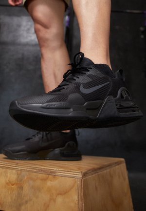 Beine in schwarzen Nike-Sneakers, die auf eine hölzerne plyometrische Kiste in einem Fitnessstudio steigen.