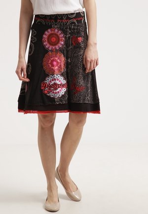 Falda negra con patrones circulares vibrantes en rojo y rosa, con un diseño texturizado y un dobladillo en contraste de color rojo. Cintura elástica.