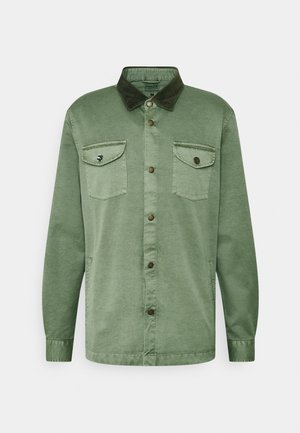 Veste chemise en coton vert avec un col en velours côtelé marron, deux poches poitrine, fermeture à boutons et manches longues. Texture lisse avec une coupe décontractée.