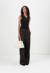 Top nero senza maniche con scollatura in pizzo, abbinato a pantaloni marroni a gamba larga a vita alta. Tiene una piccola borsa color crema.