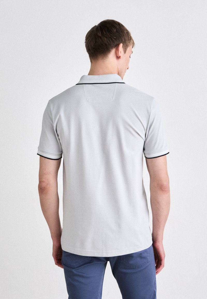 Polo gris clair à manches courtes, avec un col et des bordures noires fines le long des manches et du col. Tissu lisse, vue arrière montrée.