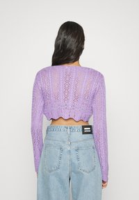 Suéter lilás curto com um padrão de malha texturizada, mangas longas e bainha em borda, combinado com jeans azuis de cintura alta com um rótulo.