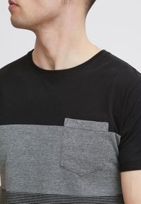 Camiseta de manga corta en negro y gris con cuello redondo, rayas horizontales y un bolsillo en el pecho de tela texturizada.