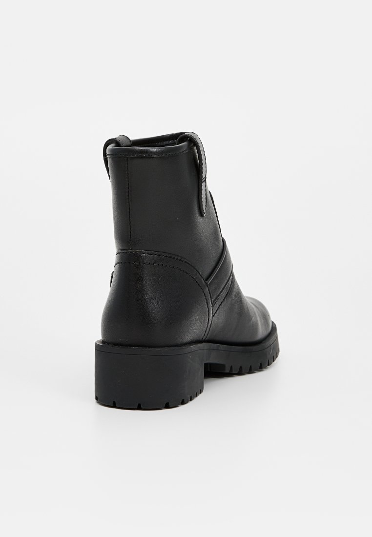 Zwarte leren enklaars met een robuuste zool, ronde neus, een lipje aan de achterkant en decoratieve stiksels aan de zijkant. Glad oppervlak overal.