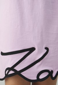 Różowy materiał o gładkiej fakturze, z wyraźnym czarnym haftem w kształcie liter "Z" i "o" na dolnym brzegu.