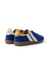 Paire de baskets en daim bleu avec des bandes blanches, des accents marron clair au talon et des semelles en caoutchouc marron, vues de dos sur fond blanc.