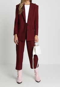 Blazer bordeaux et pantalon assorti en tissu texturé, associés à un haut blanc, des bottes roses et un petit sac à main blanc.
