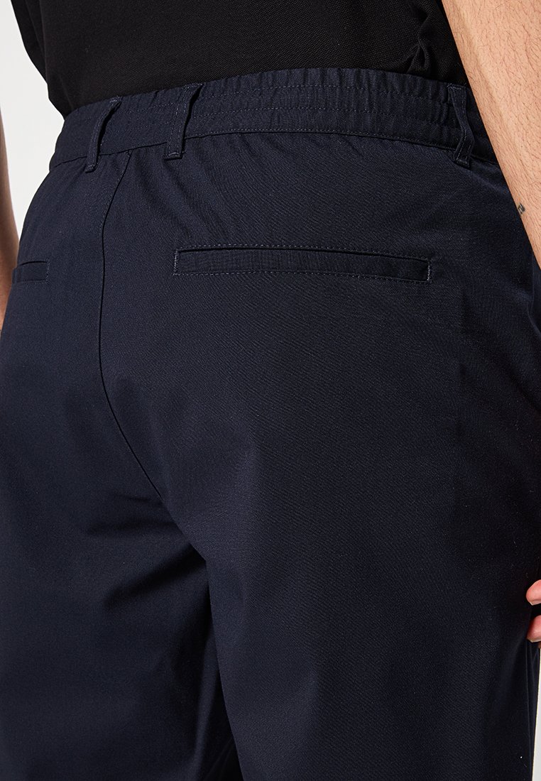 Marineblaue Hose aus strukturiertem Stoff, mit elastischem Bund und Gesäßtaschen. Mit taillierter Passform und glatter Oberfläche.