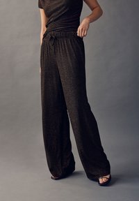 Čierne nohavice s širokými nohavicami vyrobené zo štruktúrovaného materiálu s kovovým leskom. Majú elastický pás s detailom na šnúrku a pohodlný voľný strih.