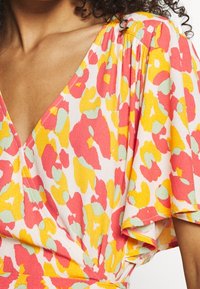 Mångfärgad klänning med v-ringning, korta fladdrande ärmar och ett blommönster i rosa, gult och mintgrönt på en ljus bakgrund.