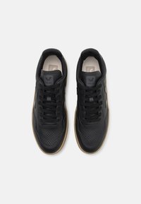 Svart lær sneakers med perforert design, svart snøring og brun gummisåle. Merkevaren er synlig på tungen.