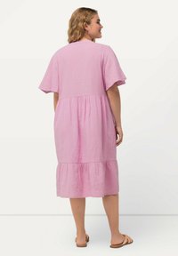 Rosa Midi-Kleid aus Baumwolle mit kurzen Ärmeln, gestuftem Design und strukturierter Stoffqualität. Mit Rundhalsausschnitt und endet knapp unter dem Knie.