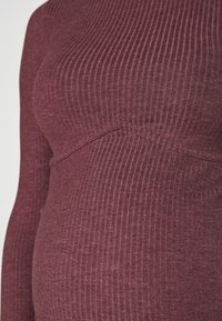 Gros plan d'un haut côtelé à manches longues couleur rose poudré, ajusté sur la poitrine et la taille avec des détails subtils de couture.