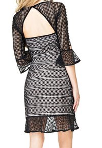 Robe en dentelle noire avec manches cloche trois-quarts, dos nu et motifs géométriques blancs sur une silhouette ajustée.