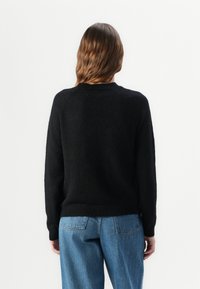 Svart, texturerad tröja med rund halsringning och långa ärmar, kombinerad med ljusblå, löst sittande jeans.