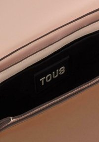 Interior de bolso de cuero rosa claro con forro oscuro, con una etiqueta TOUS. La textura suave y los detalles de costura limpia realzan el diseño.