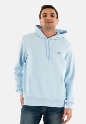 Sudadera azul claro hecha de tela suave, con un bolsillo canguro, capucha con cordón y un pequeño logo verde en el pecho.