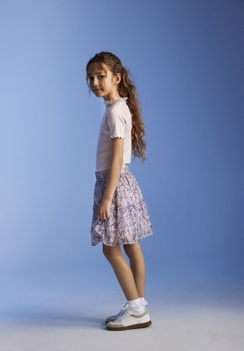 Lyserød ribbet top med blonder, parret med en blomsterprintet nederdel i pastelfarver. Hvide sneakers med lacesokker fuldender outfittet.