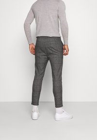 Szare spodnie w kratę o dopasowanym kroju i zwężanych nogawkach, wykonane z lekkiego materiału, zestawione z białymi trampkami.