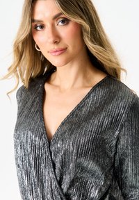 Metallic silver wrap top with a textured, vertical pleated design. Features a deep V neckline and a soft, flowing fabric.