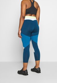 Legginsy z wysokim stanem w ciemnym odcieniu teal z kontrastującymi panelami w jasnym niebieskim i białym kolorze. Wykonane z elastycznego materiału dla komfortu i swobody ruchów.