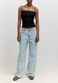 Schwarzes, geripptes Tanktop mit dünnen Trägern, kombiniert mit hellblauen weit geschnittenen Jeans. Schwarze Sandalen mit dekorativen Akzenten runden das Outfit ab.