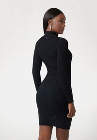 Black ribbed dress with a fitted silhouette, high neck, long sleeves, and a textured pattern, featuring a subtle detail at the hem.