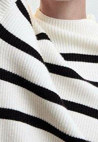 Czarny i biały sweter z prążkowanym wzorem i wysokim kołnierzem. Paski mają różne szerokości.