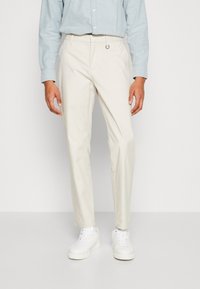 Pantaloni beige chiaro realizzati in tessuto resistente, design a gamba dritta, con un passante in vita, abbinati a sneaker bianche.