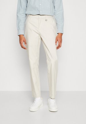 Pantaloni beige chiaro realizzati in tessuto resistente, design a gamba dritta, con un passante in vita, abbinati a sneaker bianche.