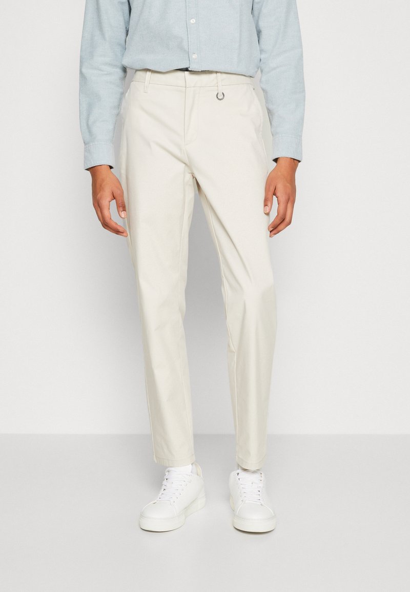 Pantaloni beige chiaro realizzati in tessuto resistente, design a gamba dritta, con un passante in vita, abbinati a sneaker bianche.