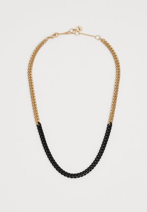 Collana in catena oro e nera con maglie spesse e un piccolo cartellino rotondo vicino al gancio su uno sfondo bianco semplice.