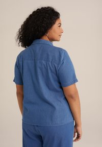 Chemise en chambray bleu à manches courtes, coupe décontractée, avec un col et une texture lisse, vue de dos.