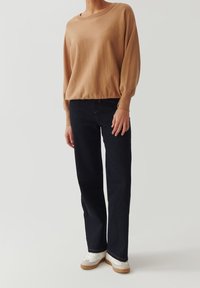 Kamelinvärinen neulepaita ilmapallohihansuilla, yhdistettynä tummiin suoralahkeisiin farkkuihin ja valkoisiin tennareihin. Yksinkertainen muotoilu ja rento istuvuus.