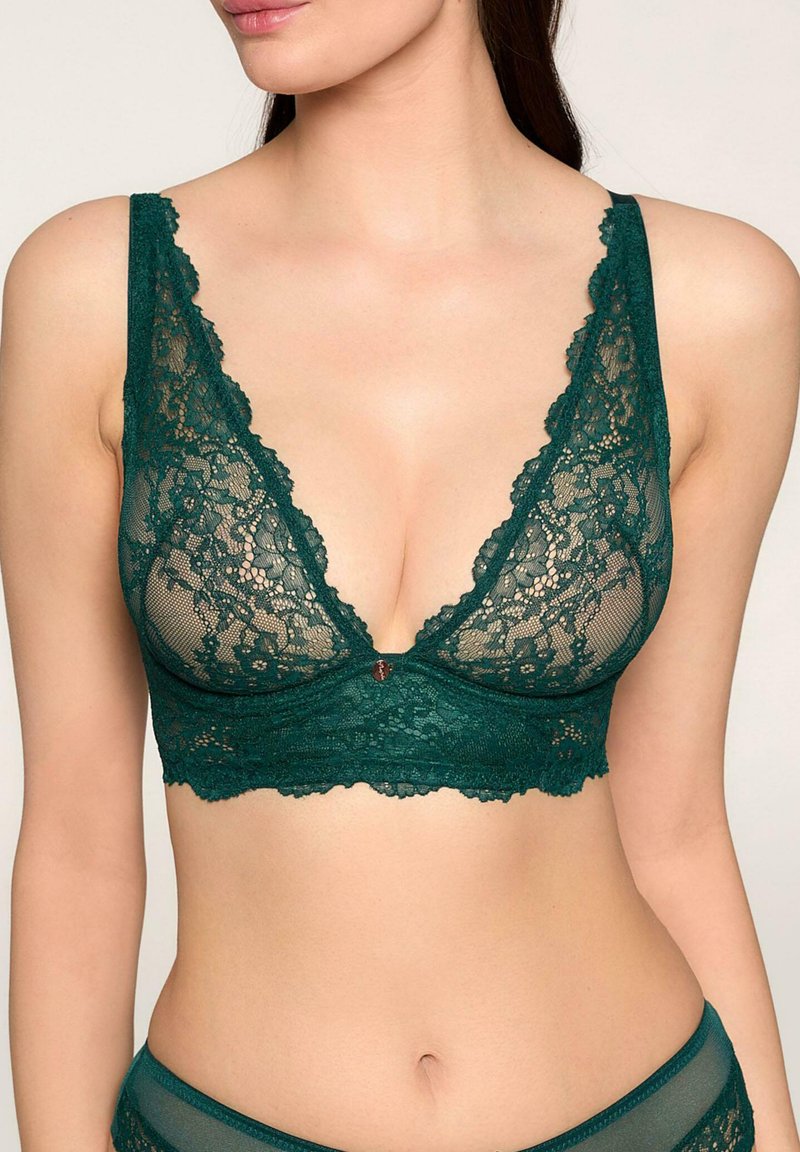 Koronkowy biustonosz w głębokim zielonym kolorze z dekoltem w serek, falbaniastymi brzegami i małym ozdobnym detalem na środku. Miękka, przezroczysta tekstura.