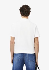 Valkoinen polo-paita, jossa on pehmeä rakenne, lyhyet hihat ja klassinen kaulus, yhdistettyinä vaaleansinisiin farkkutilkoihin.